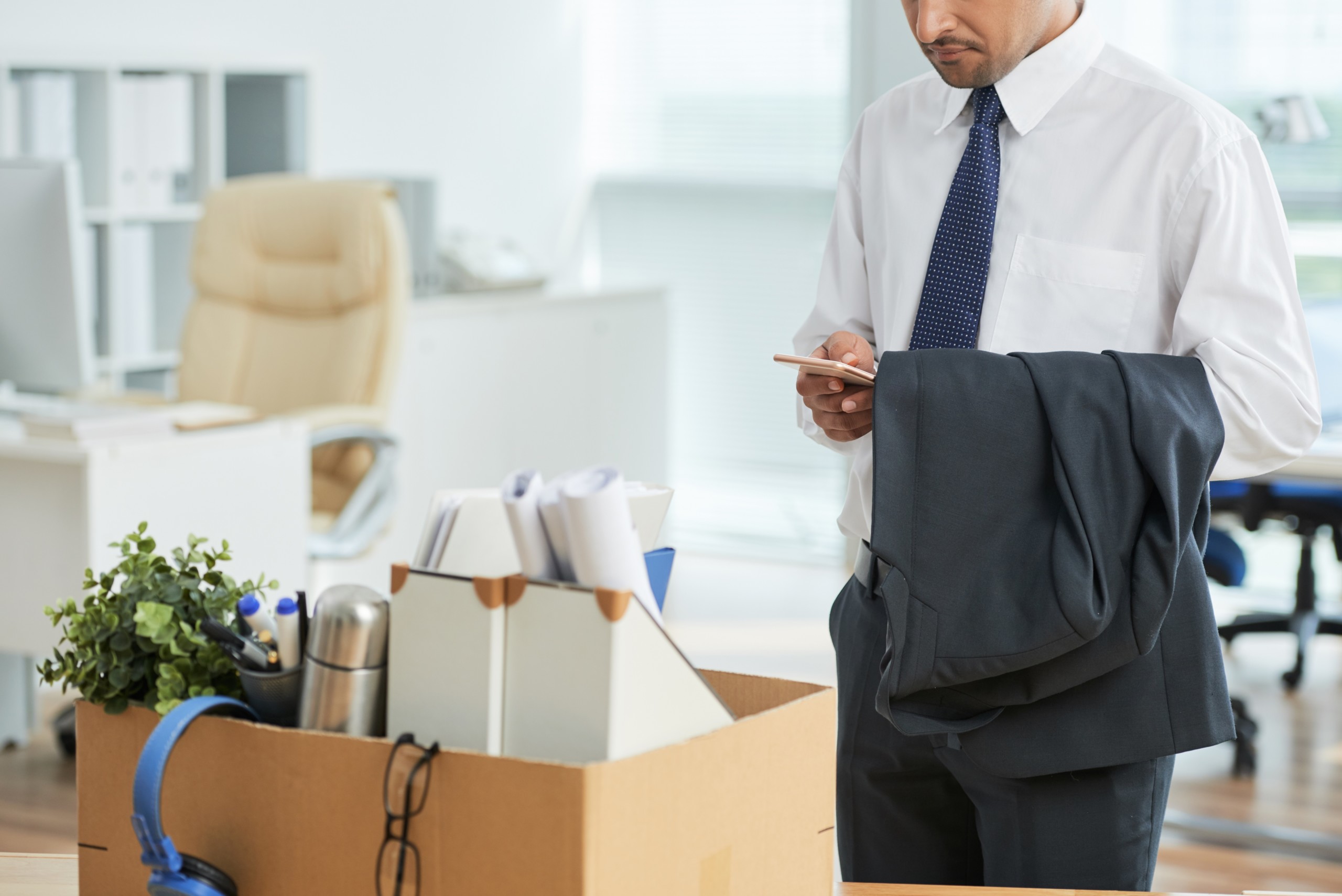 unrecognizable-man-standing-office-using-smartphone-with-personal-belongings-box